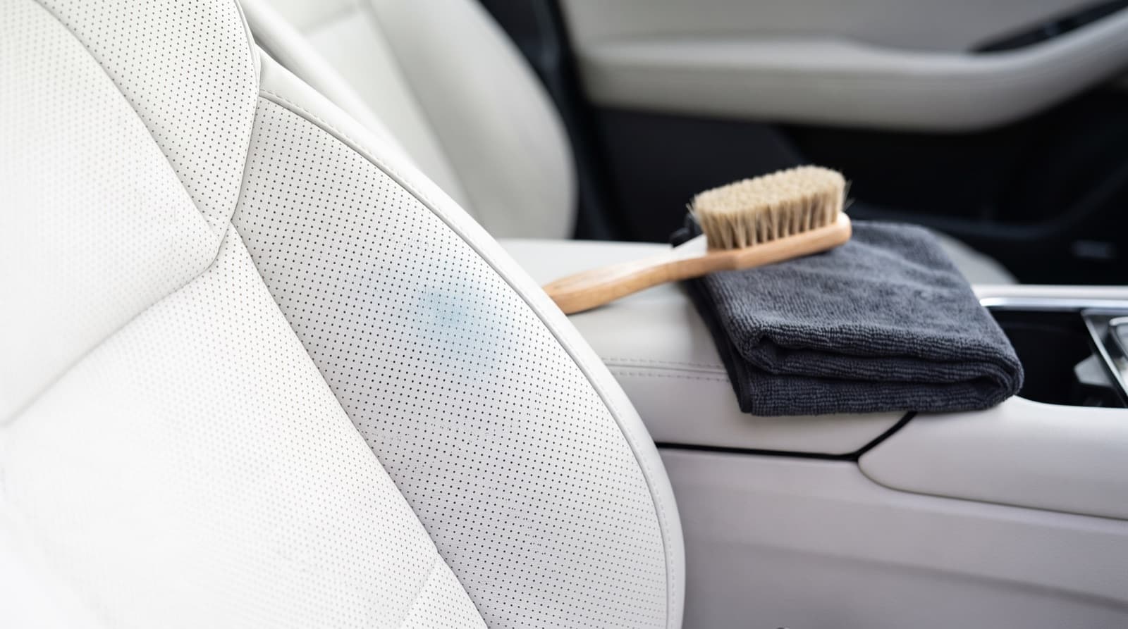 Microfiber cloth wiping a faint blue jean dye mark off a white Tesla vegan leather front seat