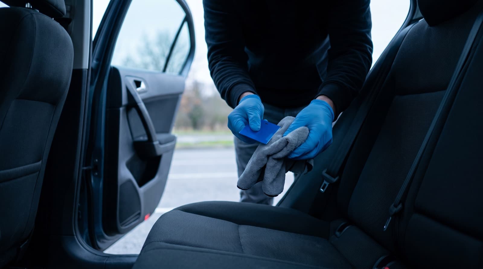 A technician in gloves cleaning a cloth back seat of a car with an enzyme spray and a wet vacuum