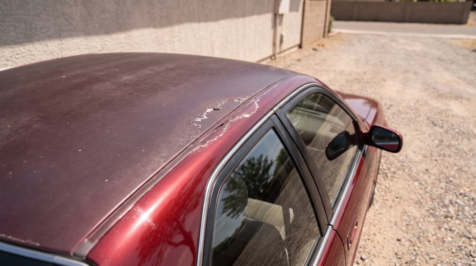 Close-up of a car roof where the clear coat is peeling in white flakes over dull, faded color paint