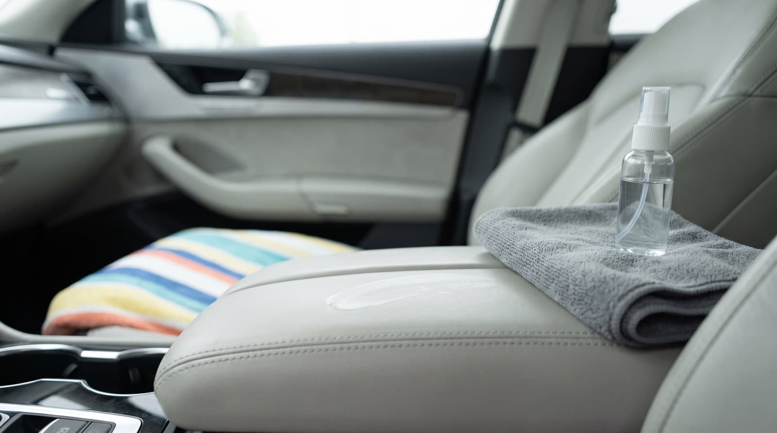 Microfiber towel wiping a white sunscreen smear off a black leather car seat bolster after a beach day