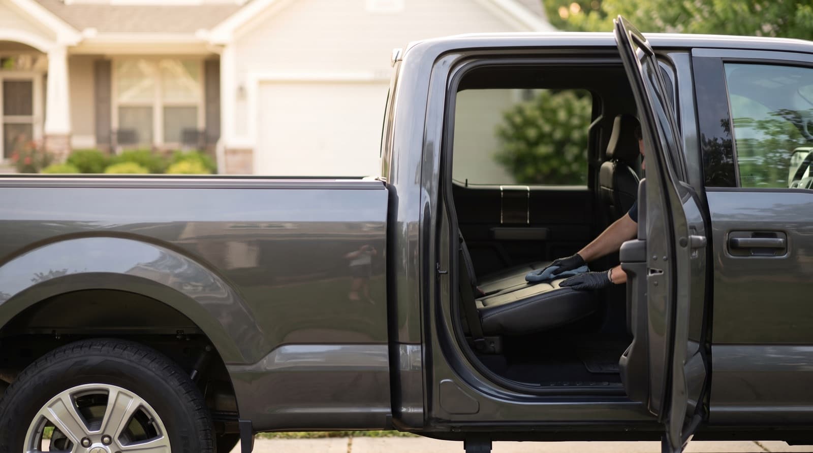A technician dries the hood of a clean gray pickup truck parked in a San Francisco driveway