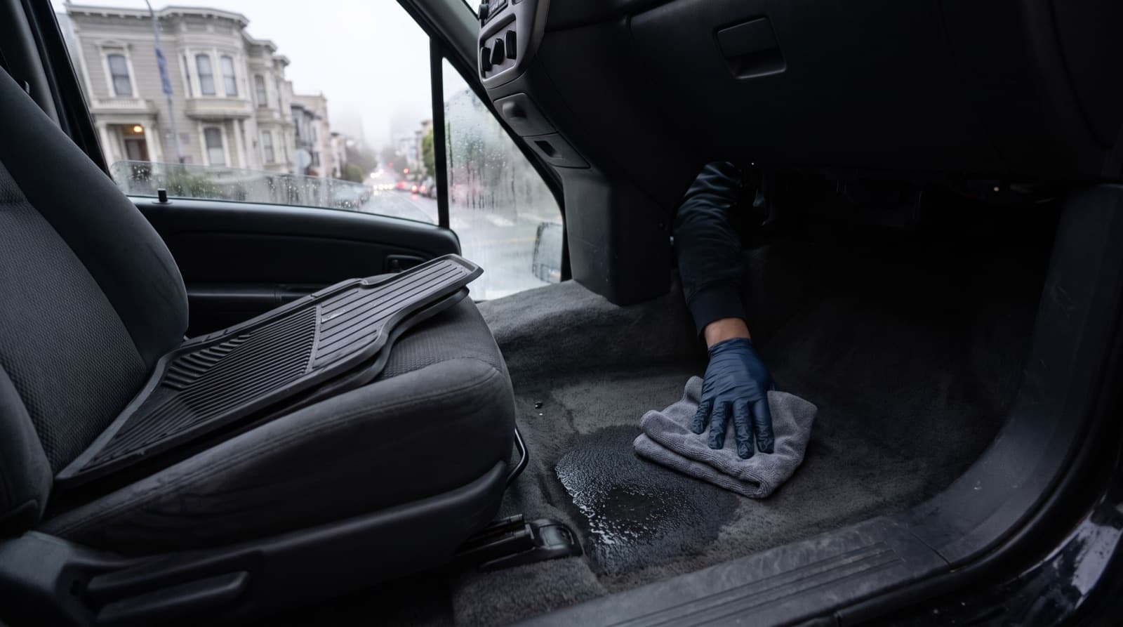 A technician uses an extractor wand to pull water out of a soaked front footwell carpet in a car with the doors open