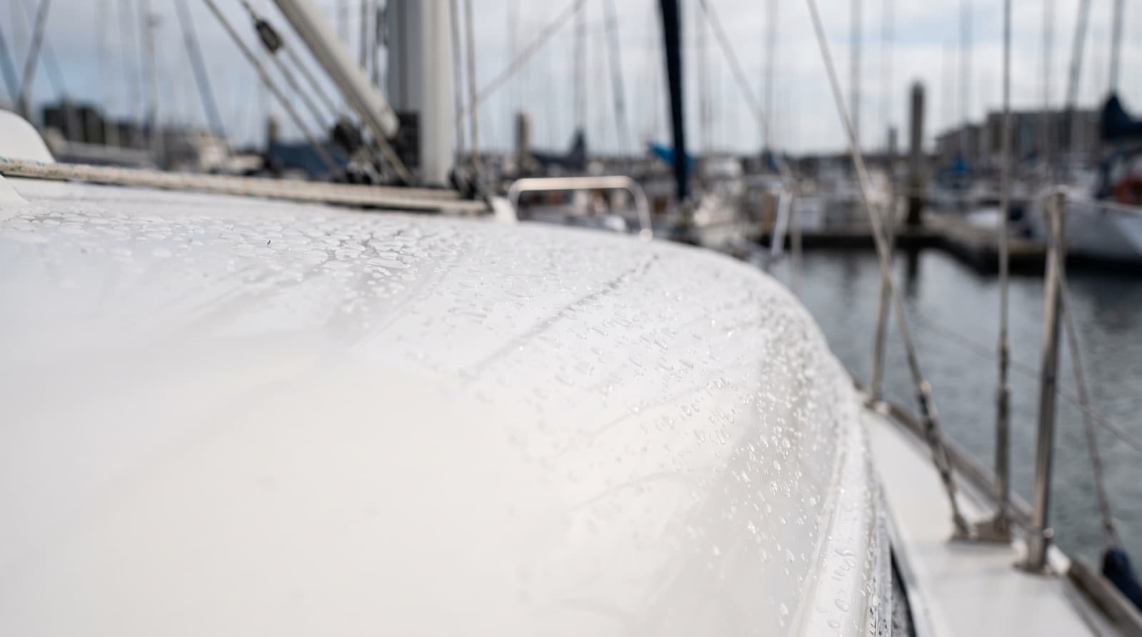 Technician wiping ceramic coating onto the dry, glossy white hull of a boat tied up at a marina slip on an overcast day