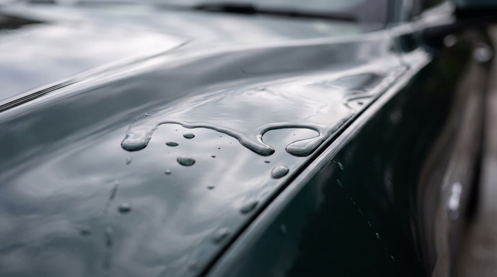 Water beading into tight round drops on the ceramic-coated hood of a dark gray car parked on a San Francisco street