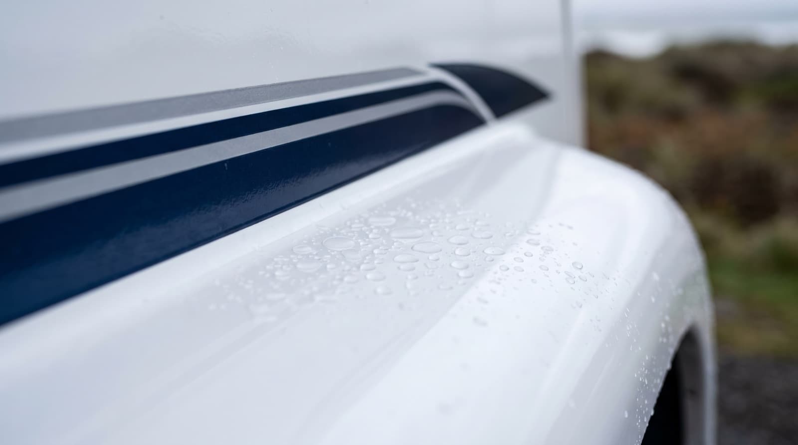 Technician polishing the white gelcoat side of a Class A motorhome before applying a ceramic coating