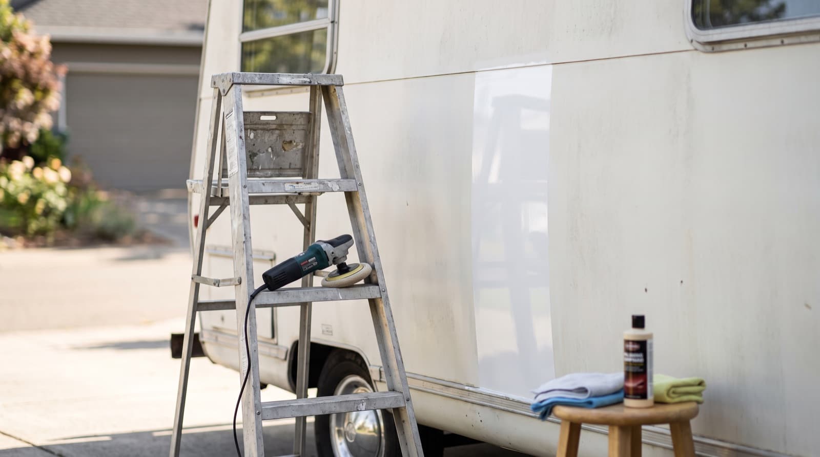 Side of a white motorhome half polished, with a dull chalky panel on one side and a glossy panel on the other, and a dark towel showing white chalk