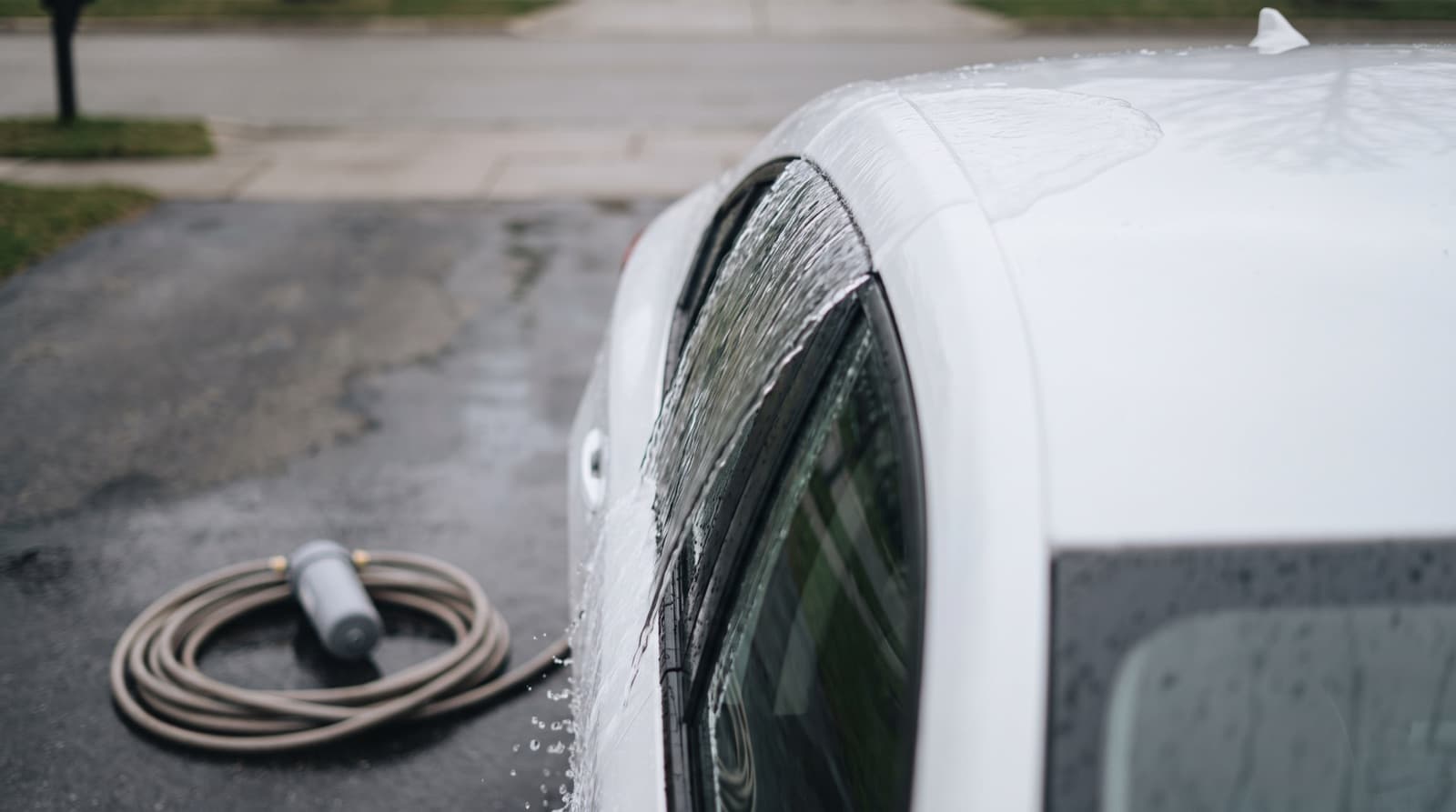 Clear water sheeting off the hood of a dark car during a final rinse, with no white spots left behind