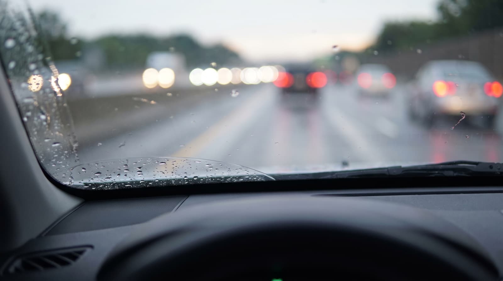 Raindrops beading on a car windshield with a small rock chip near the edge, on a foggy Bay Area morning